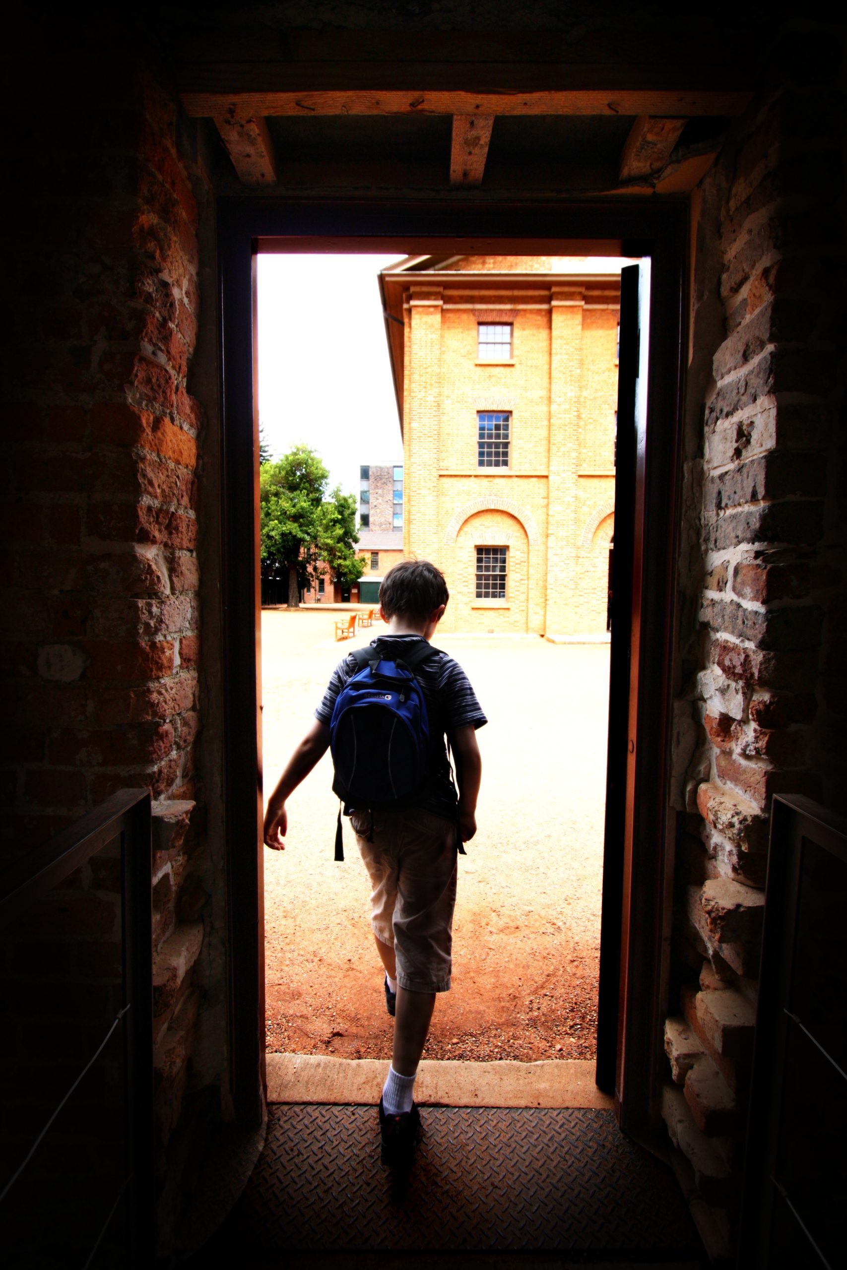 boy carrying a rucksack walking through a doorway into the light